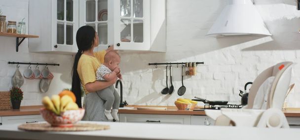 Young mother doing housework while holding baby - 写真・画像