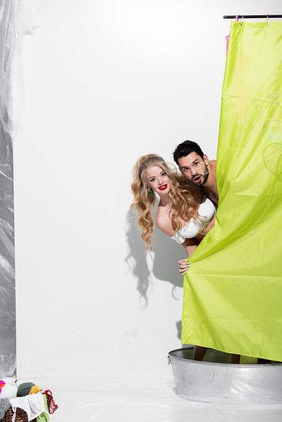 feliz pin up mujer y hombre sorprendido cubriendo con cortina de ducha en blanco
 - Foto, imagen
