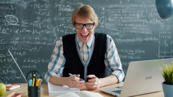 Portrait of happy young man crazy scientist laughing in class at desk looking at camera - Imágenes, Vídeo