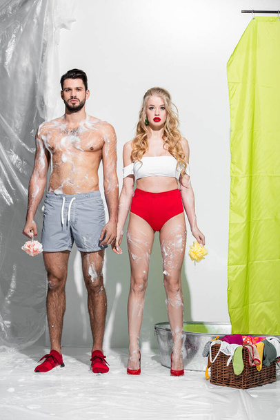 sexy Pin Up Mädchen hält nassen Schwamm mit Seife in der Nähe hemdlosen Mann auf weiß  - Foto, Bild