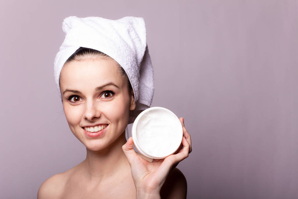 girl with a white towel on her head and a can of cream in her hands, gray background - Foto, Imagem