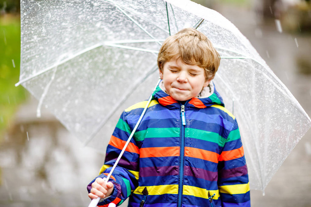Όμορφο αγοράκι στο δρόμο για το σχολείο περπατώντας κατά τη διάρκεια του ύπνου, της βροχής και του χιονιού με μια ομπρέλα την κρύα μέρα. Ευτυχισμένο και χαρούμενο παιδί με πολύχρωμα casual ρούχα μόδας. - Φωτογραφία, εικόνα