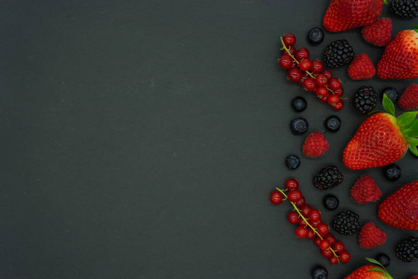 Black background with currants, blueberries, strawberries, raspberries and blackberries on the right side of the image with space for text on the left. Healthy food concept. - Photo, Image