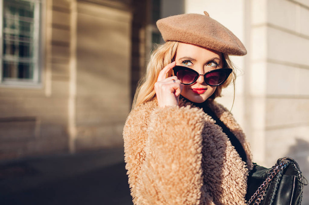 Weibliche Frühjahrsmode. Stilvolle Frau mit Kleidung, Accessoires Baskenmütze, Sonnenbrille, Mantel mit Handtasche. Außenporträt - Foto, Bild