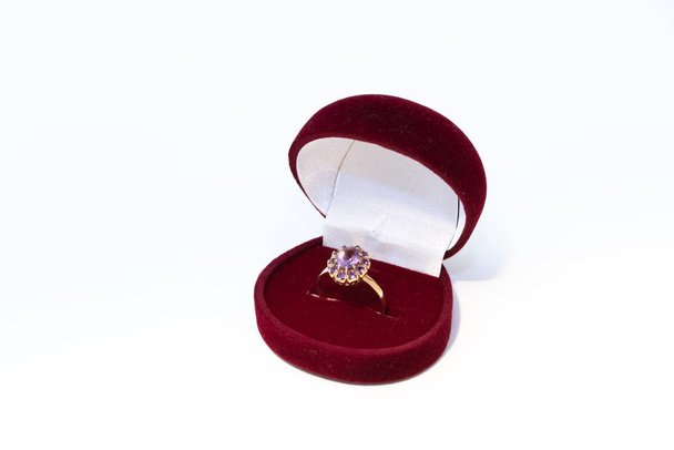Gouden ring met paarse edelsteen in een rode sieradendoos op witte achtergrond - Foto, afbeelding