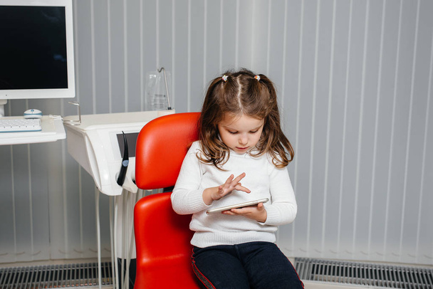 In dentistry, a little girl plays with her phone. Dentistry - Фото, зображення