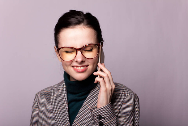 girl in a green turtleneck, jacket, glasses talking on the phone portrait on a gray background - Photo, image