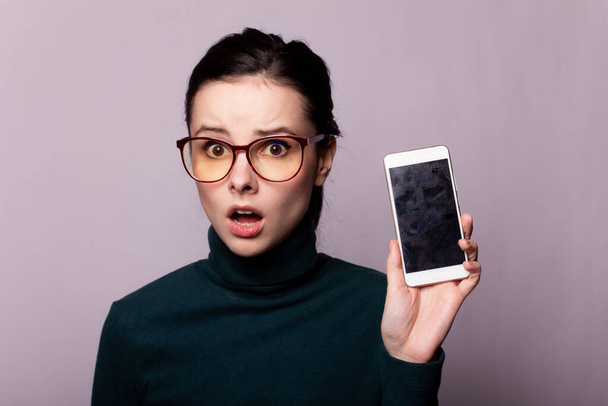 dívka v zeleném roláku a brýle pro zrak komunikuje na telefonu, portrét na šedém pozadí - Fotografie, Obrázek
