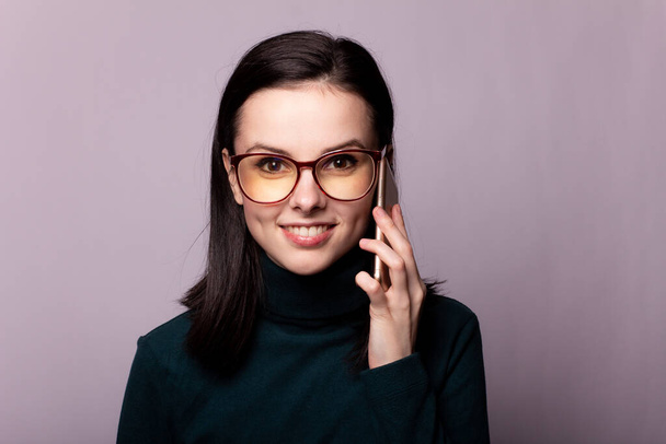girl in a green turtleneck and glasses for sight communicates on the phone, portrait on a gray background - Valokuva, kuva