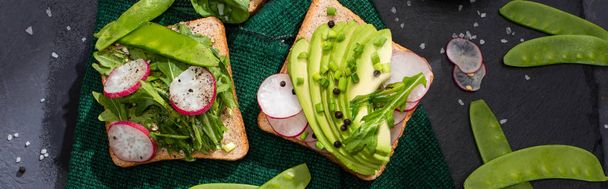 panoramatický záběr vegetariánských sendvičů s ředkvičkami, hráškem a avokádem na plátně - Fotografie, Obrázek