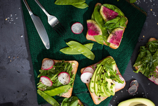 top view of vegetarian healthy toasts with fresh vegetables on cloth with fork and knife - Photo, Image