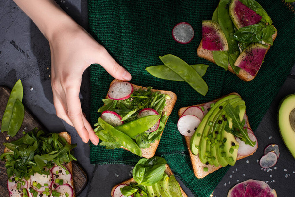 cropped view of woman taking sandwiches with radish, green peas and avocado - Φωτογραφία, εικόνα