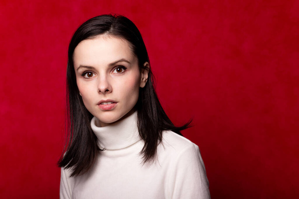 girl in a white turtleneck, portrait on a red background - 写真・画像