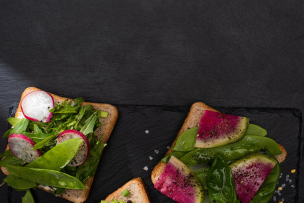 top view of organic toasts with vegetables on stone board with pepper and salt - Photo, Image