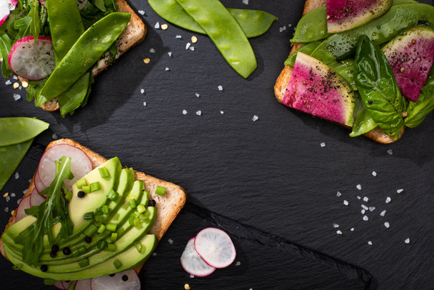vrchní pohled na vegetariánské toasty se zeleninou na kamenné desce s pepřem a solí - Fotografie, Obrázek