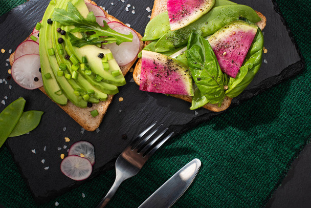 top view of vegetarian sandwiches with fresh vegetables on cloth and stone board with fork and knife - Foto, afbeelding