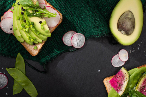 top view of fresh toasts with radish, green peas, leek and avocado on green cloth - Photo, image