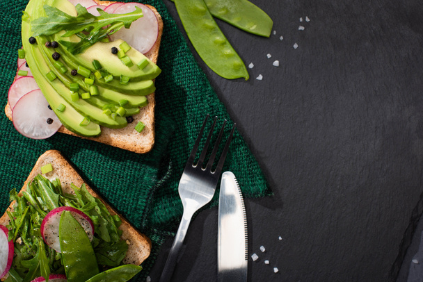 top view of vegetarian organic toasts with fresh vegetables on cloth with fork and knife - Photo, Image