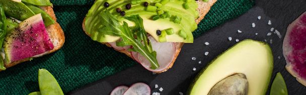 panoramic shot of fresh toasts with radish and avocado on green cloth - 写真・画像