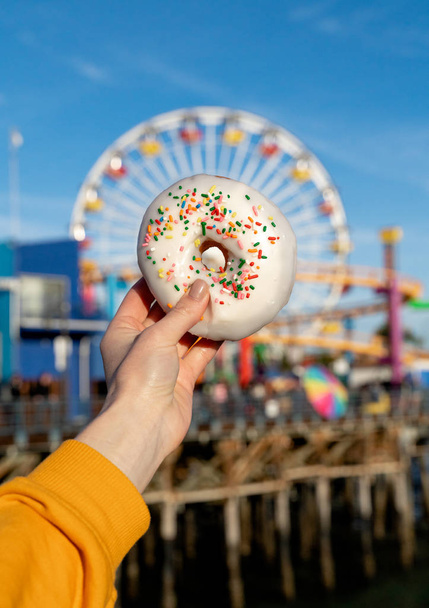 Female hand holding a donut on a background of a ferris wheel - Photo, Image