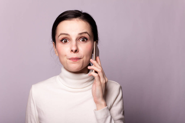 girl in a white turtleneck talking on the phone, portrait on a gray background - Foto, Imagen