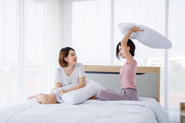 Two girl play pillow fighting in bright bedroom. Concept teenage lifestyle. - Foto, afbeelding