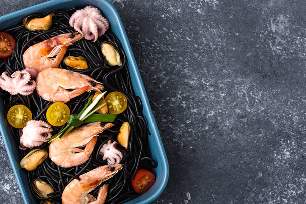 plato inusual de espagueti negro con tinta de sepia con mariscos y verduras en plato azul sobre fondo gris, concepto de cocina mediterránea
 - Foto, Imagen