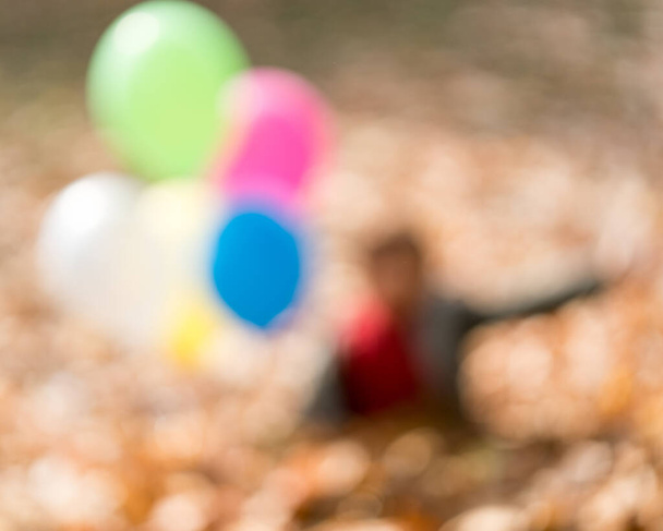 Blurred photo of child in autumn leaves with balloons - Foto, immagini