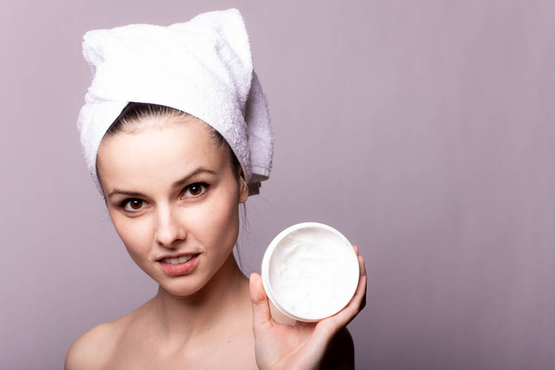 girl with a white towel on her head and a can of cream in her hands, gray background - Foto, Imagem