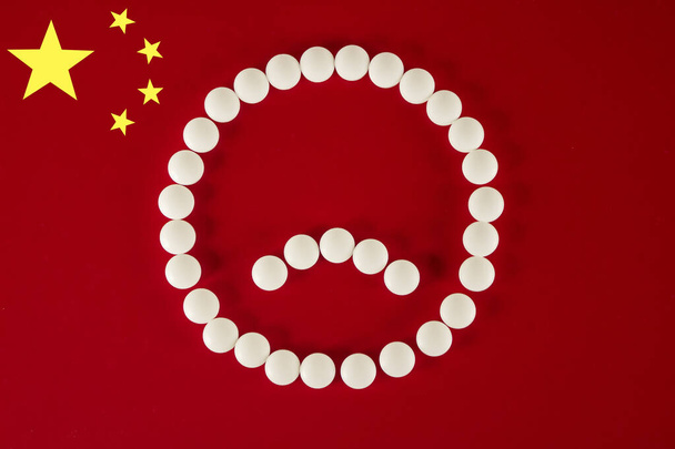 Triste visage souriant fait de comprimés blancs et de pilules sur fond rouge du drapeau chinois, vue de dessus. Nouveau Coronavirus 2019 Concept 2019-nCoV
 - Photo, image
