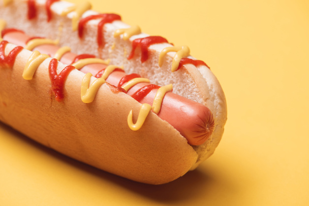 close up of one hot dog with sausage, mustard and ketchup on yellow - Zdjęcie, obraz