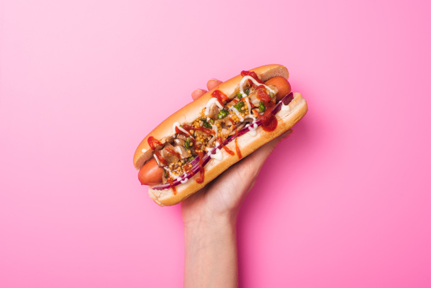 partial view of woman holding yummy hot dog in hand on pink - Фото, изображение