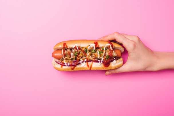 partial view of woman holding one tasty hot dog on pink - Foto, Imagem