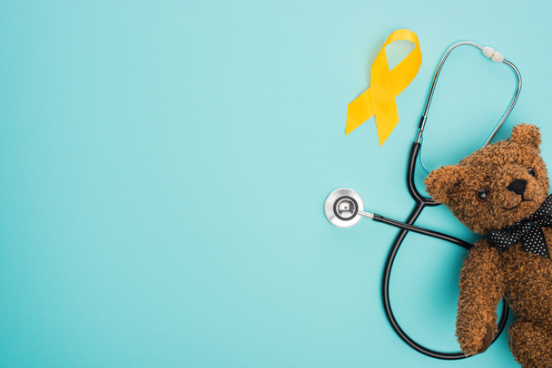 青い背景に黄色のリボン、おもちゃ、聴診器のトップビュー、国際小児がんの日の概念 - 写真・画像
