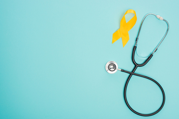 Widok z góry żółtej wstążki ze stetoskopem na niebieskim tle, koncepcja międzynarodowego dnia nowotworu w dzieciństwie - Zdjęcie, obraz
