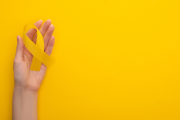 Częściowy widok kobiecej ręki z żółtą wstążką na kolorowym tle, koncepcja międzynarodowego dnia nowotworu w dzieciństwie  - Zdjęcie, obraz