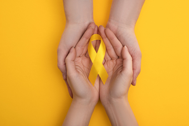Oříznutý pohled na pár držící žlutou stuhu na barevném pozadí, mezinárodní koncepce dne rakoviny v dětství - Fotografie, Obrázek