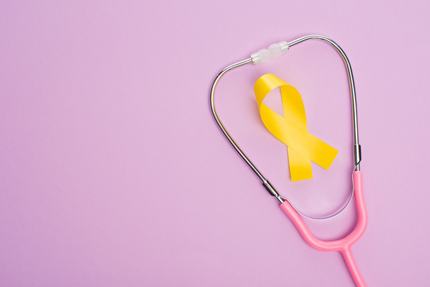 Widok z góry żółtej wstążki i różowego stetoskopu na fioletowym tle, koncepcja międzynarodowego dnia nowotworu w dzieciństwie - Zdjęcie, obraz