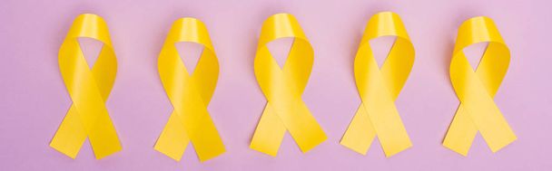 Flat lay with yellow awareness ribbons on violet background, panoramic shot, international childhood cancer day concept - Foto, Imagen