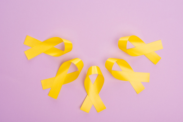 Flat lay with yellow ribbons on violet background, international childhood cancer day concept - Foto, Imagem