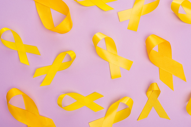 Top view of yellow ribbons on violet background, international childhood cancer day concept - Фото, изображение