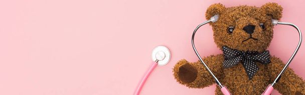 Top view of stethoscope connected with teddy bear on pink background, panoramic shot, international childhood cancer day concept - Photo, Image