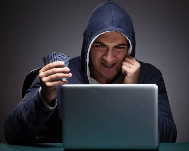 Egy kapucnis fiatalember ül egy laptop előtt. - Fotó, kép