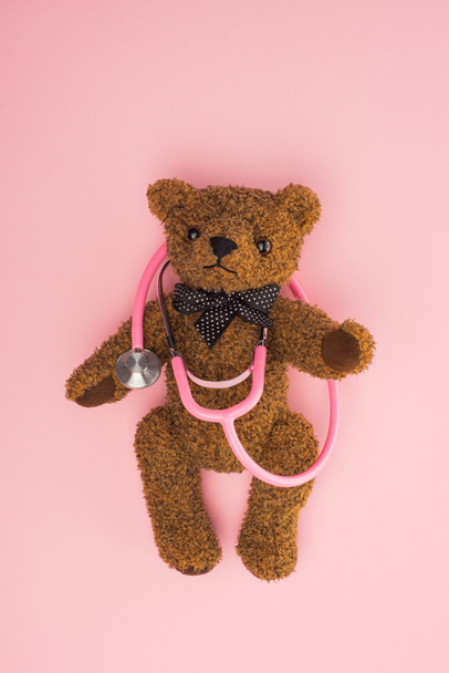 Top view of brown teddy bear with stethoscope on pink, international childhood cancer day concept - Foto, imagen