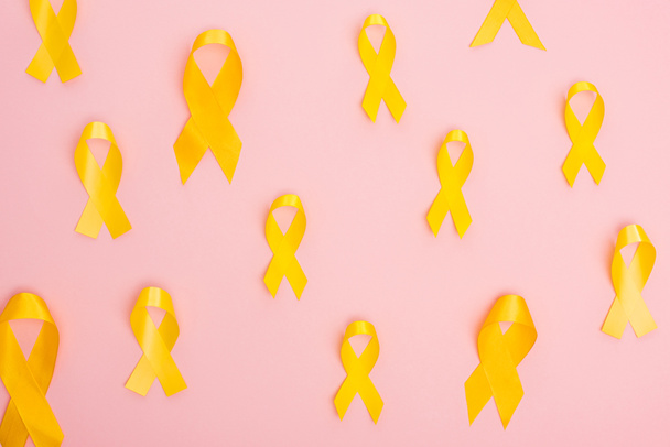 Widok z góry żółte wstążki na różowym tle, międzynarodowa koncepcja dzień nowotworu dzieciństwa - Zdjęcie, obraz