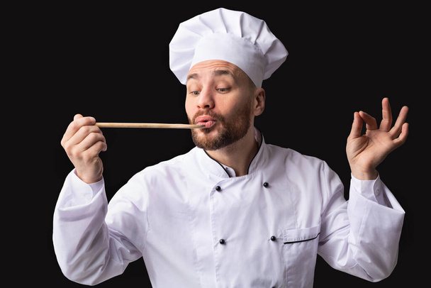 Cook Man Tasting Dish Over Black Studio Background - Photo, Image