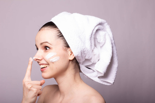 girl with a white towel on her head and cream on her face and hand, gray background - Foto, imagen