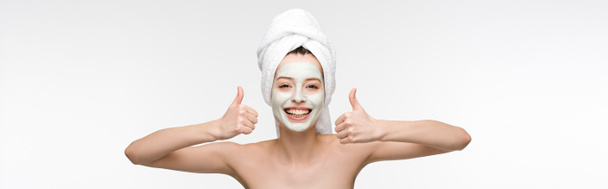 tiro panorâmico de menina feliz com máscara facial nutritiva e toalha na cabeça mostrando polegares isolados no branco
 - Foto, Imagem