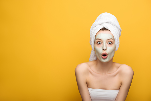 shocked girl with nourishing facial mask and towel on head looking at camera on yellow background - Foto, Bild