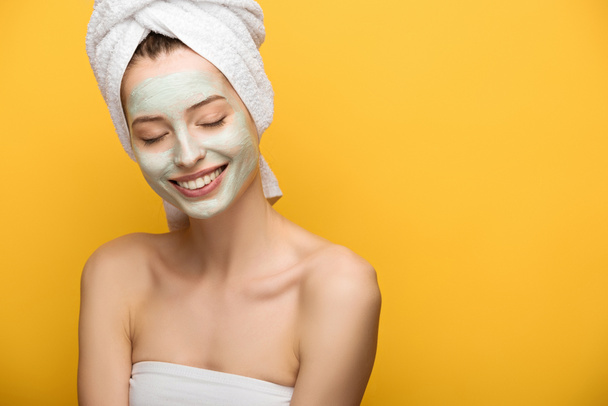 smiling girl with nourishing facial mask standing with closed eyes isolated on yellow - Photo, Image